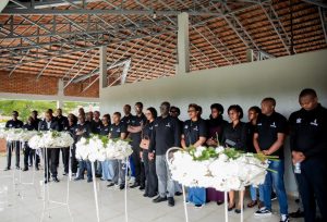 Group of mourners in black, lined up behind white flower arrangements in a covered outdoor venue