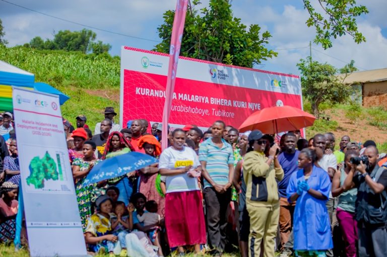 Crowd of people at an outdoor health outreach event with a red banner and informational signs on display.