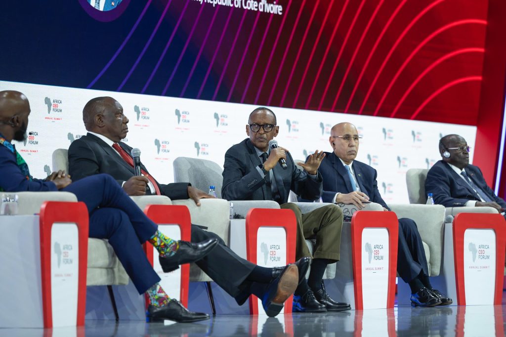 Panel of five business leaders in suits seated on stage at the Africa CEO Forum, microphones in hand, backdrop with logos behind them.