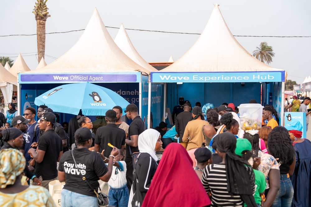 Crowd of people at a Wave Experience Hub booth with blue tents and white canopies at an outdoor event.