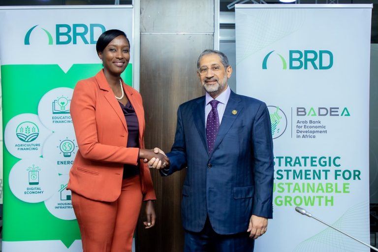 Two business professionals shake hands in front of BRD banners at a formal event with smiles on their faces.