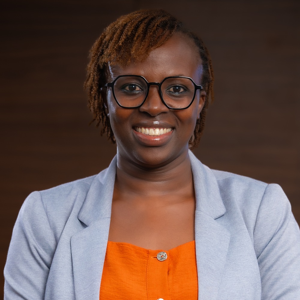 Portrait of a smiling woman wearing glasses, a light blue blazer, and an orange top, looking straight at the camera.