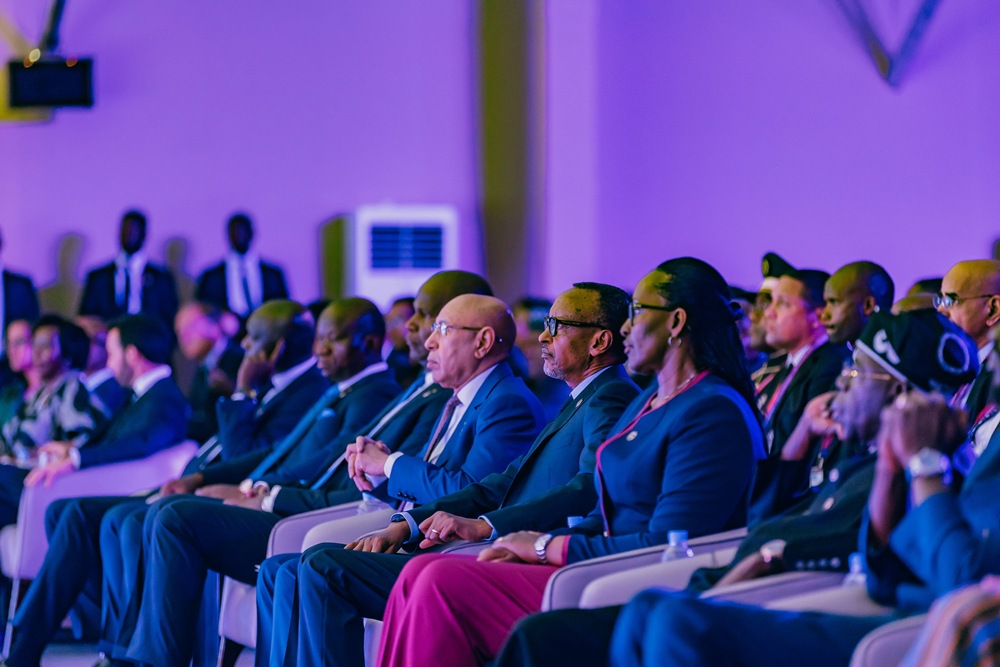 Audience of diverse professionals seated in rows at a conference, listening to a speaker in a purple-lit room.