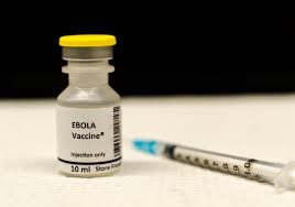 Vial labeled Ebola Vaccine beside a syringe on a white surface.