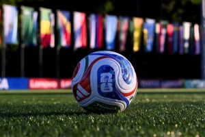 Soccer ball with blue, red, and white patterns on a grass field with blurred colorful flags in the background