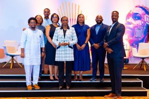 Eight diverse professionals pose on a stage for a group photo at an event, smiling at the camera.