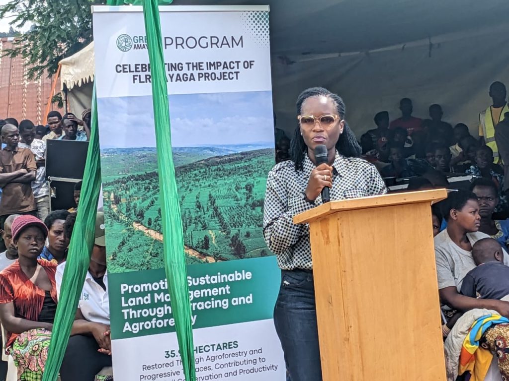 Female speaker at a wooden lectern addressing an outdoor audience, with a banner about sustainable land management behind her.