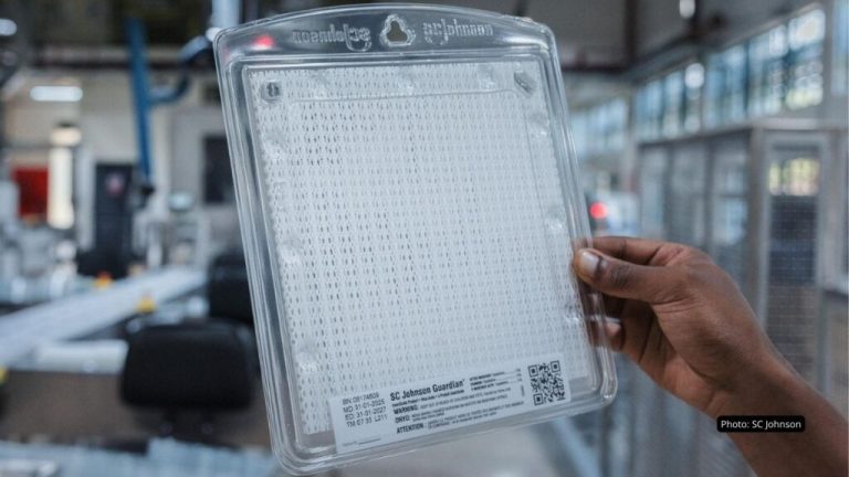 Hand holding a large clear plastic package with a grid pattern and a small QR code label at the bottom.