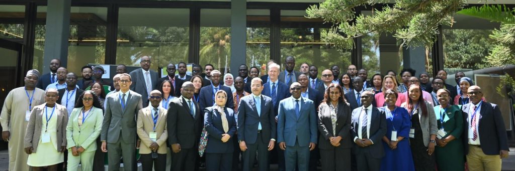 A large diverse group of professionals in business attire posing for a group photo outside a glass-front building, many wearing lanyards and badges.