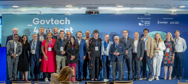 Group of diverse professionals posing for a photo on stage at a Govtech event, blue banner behind them on the backdrop.