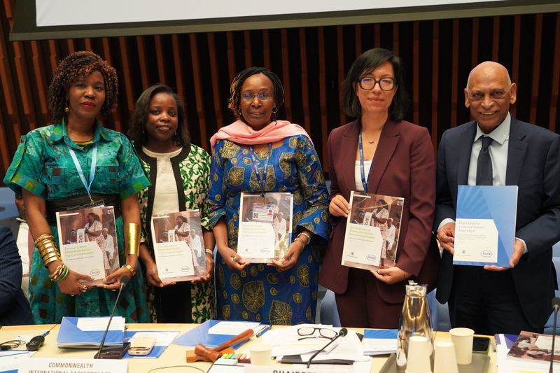Five professionals in business attire stand behind a conference table, each holding a booklet or document and posing for the photo.