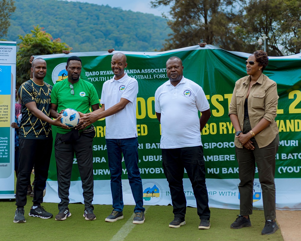 Group of five people standing on a football field in front of a green banner, posing with a ball for a sports event.