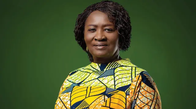 Portrait of a woman with short curly hair wearing a vibrant patterned dress against a solid green background.