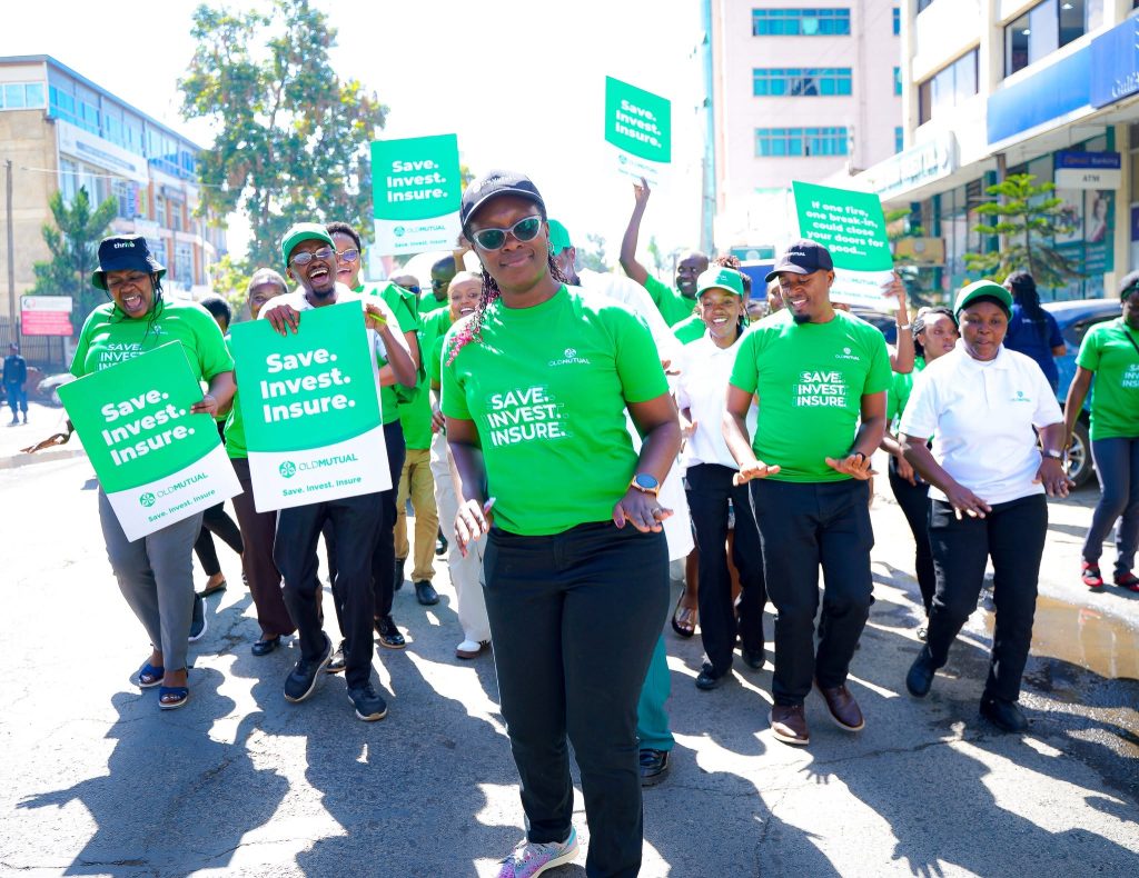 Group of people in green shirts marching on a sunny urban street, holding signs that read 'Save. Invest. Insure.'