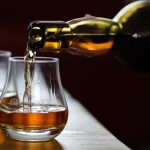 Whiskey being poured from a bottle into a short glass on a wooden bar with amber liquid mid-pour