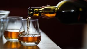 Whiskey being poured from a bottle into a short glass on a wooden bar with amber liquid mid-pour