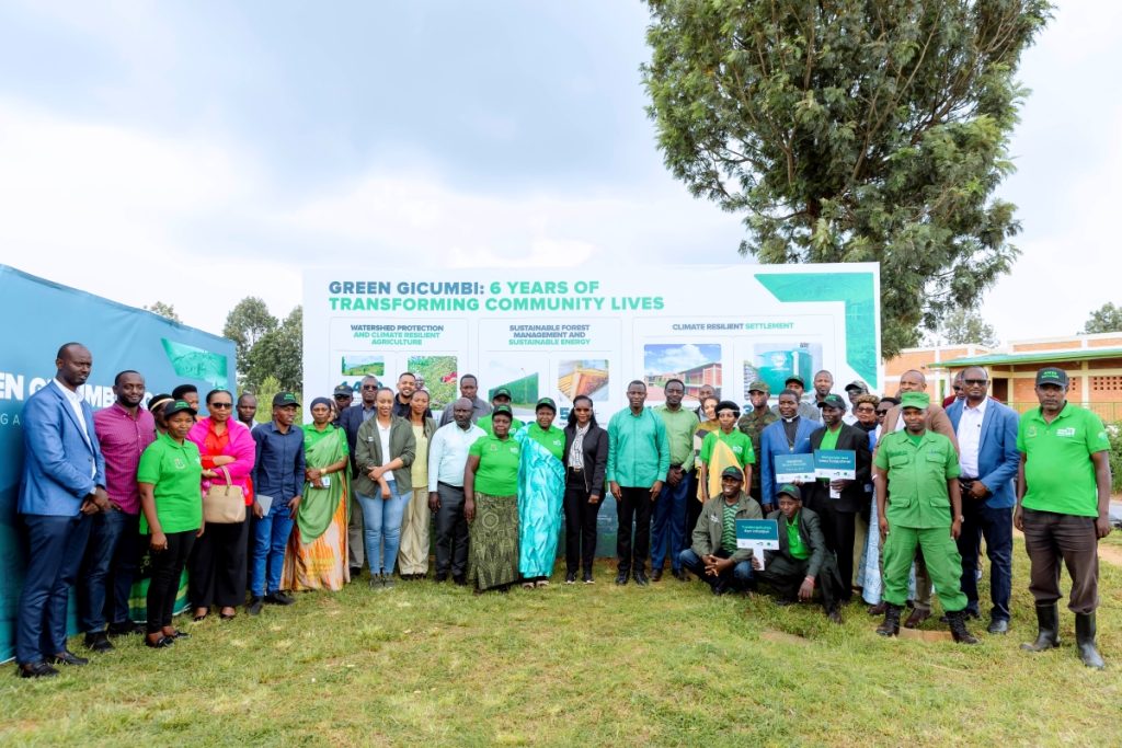 Group photo of community members and officials at a Green Gicumbi event outdoors, standing in front of a banner about transforming community lives.