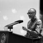 African American man wearing glasses speaking at a podium with multiple microphones at a press conference (black and white).