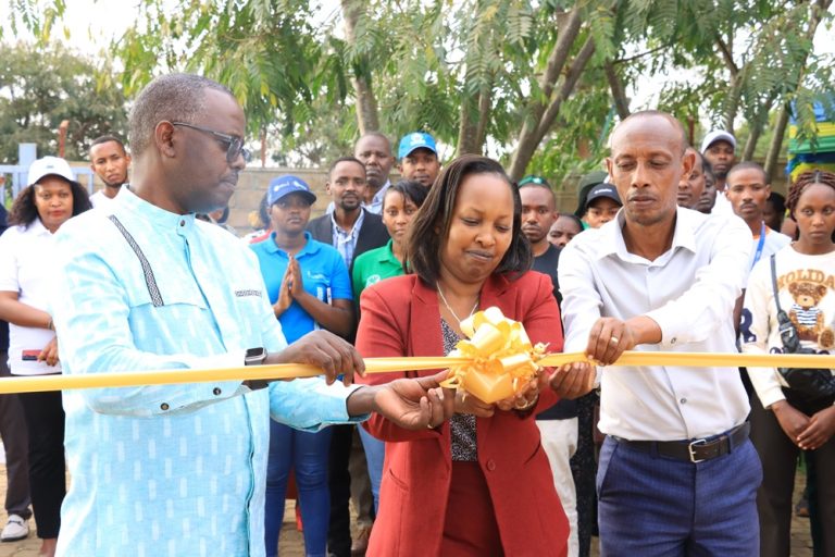 Group of three people cutting a yellow ribbon at an outdoor ceremony, with a cheering crowd in the background and a bright yellow bow in the center.
