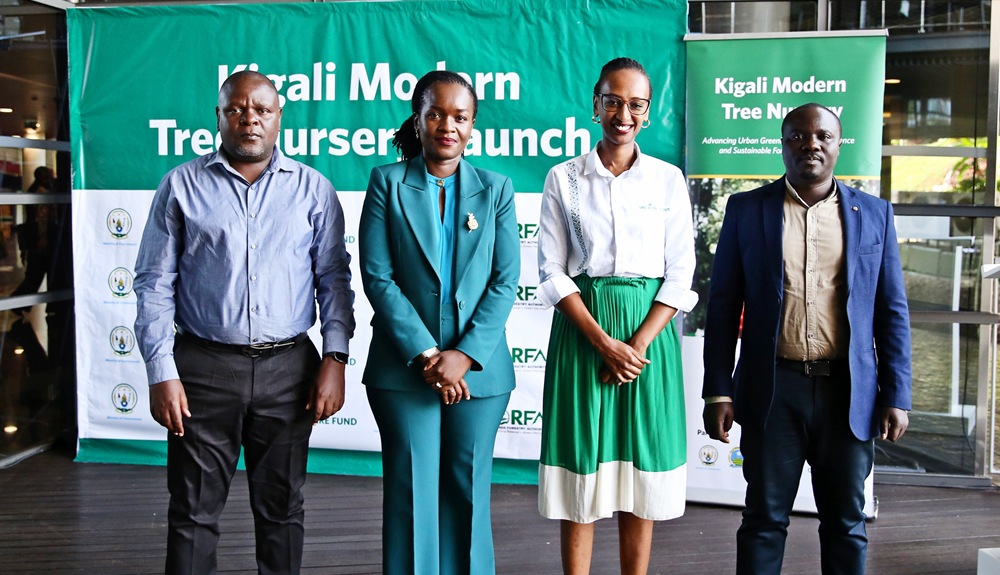 Four professionals stand in a row at a Kigali Modern Tree Nursery Launch, in front of a green event banner.