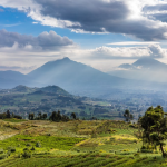 Terraced green fields in foreground with rolling hills and misty mountains beneath a cloudy sky.