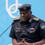 Police officer in dark uniform speaking into a microphone at a podium against a blue backdrop.