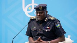 Police officer in dark uniform speaking into a microphone at a podium against a blue backdrop.