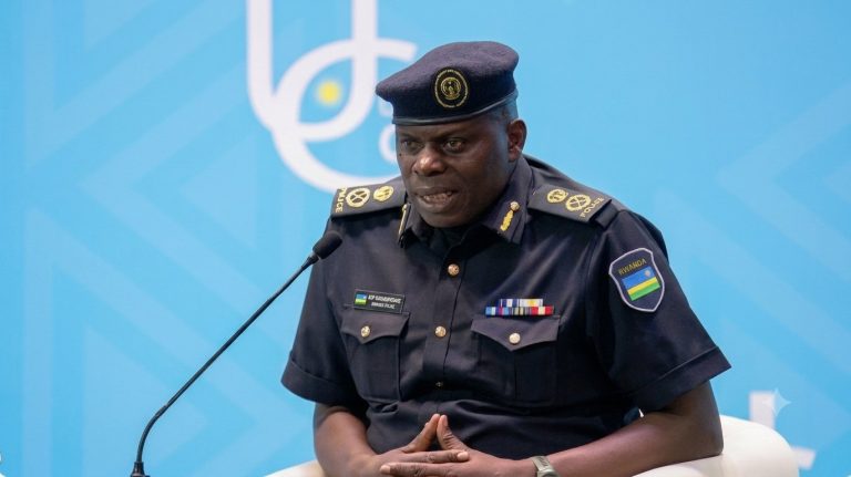 Police officer in dark uniform speaking into a microphone at a podium against a blue backdrop.
