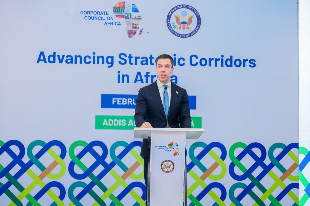 Man in a suit giving a speech at a podium with a banner reading 'Advancing Strategic Corridors in Africa' and logos of the Corporate Council on Africa behind him, outdoor event setting.