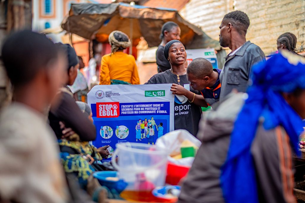 People in a crowded marketplace gather around an Ebola awareness poster to learn about prevention and protection of communities