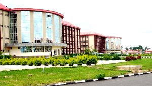 Modern campus building with curved glass facade and red roofs, surrounded by green landscaping and a paved road in foreground.