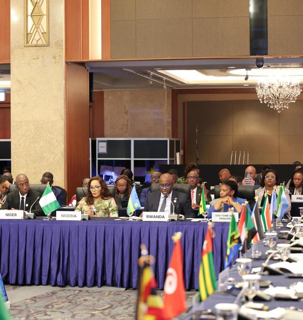 International conference with delegates seated at a long blue-clothed table, flags of various nations in front of them.