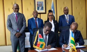 Two men seated at a table sign documents while four officials stand behind them in a formal office; flags of Kenya and Senegal on the table.
