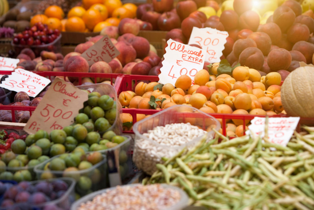 Assorted fresh fruit at a busy market stall with handwritten price tags in euros.