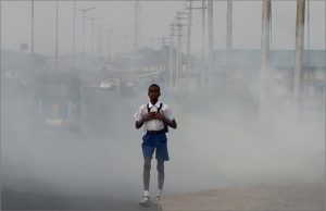 Boy in a school uniform walks along a smoke-filled street with vehicles fading in the hazy background.