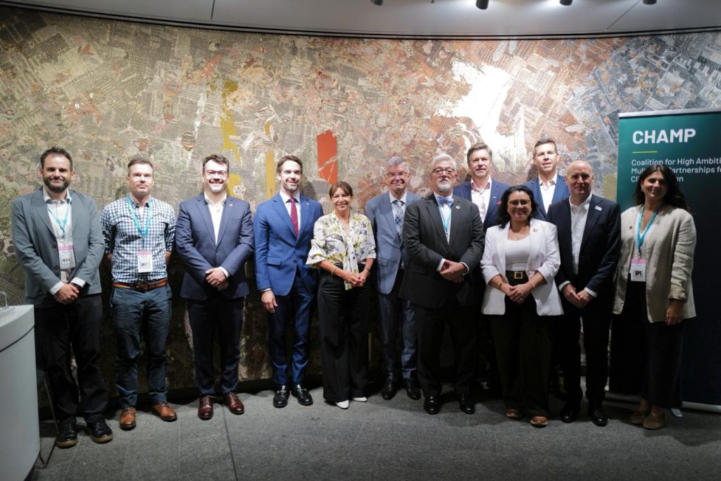 Group of professionals in business attire posing for a photo at a conference, in front of an abstract wall and a CHAMP banner to the right.