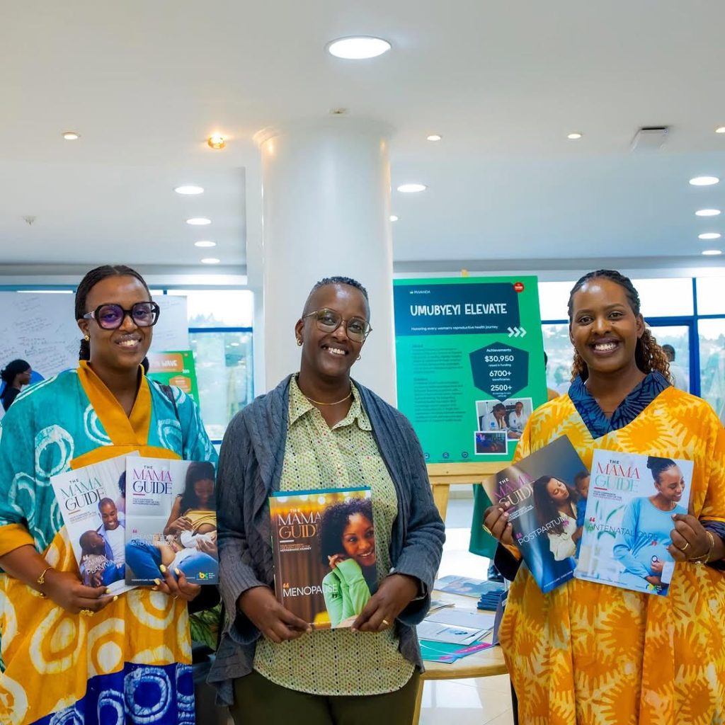 Three women stand indoors, smiling, each holding colorful magazines labeled 'Mama Guide'.