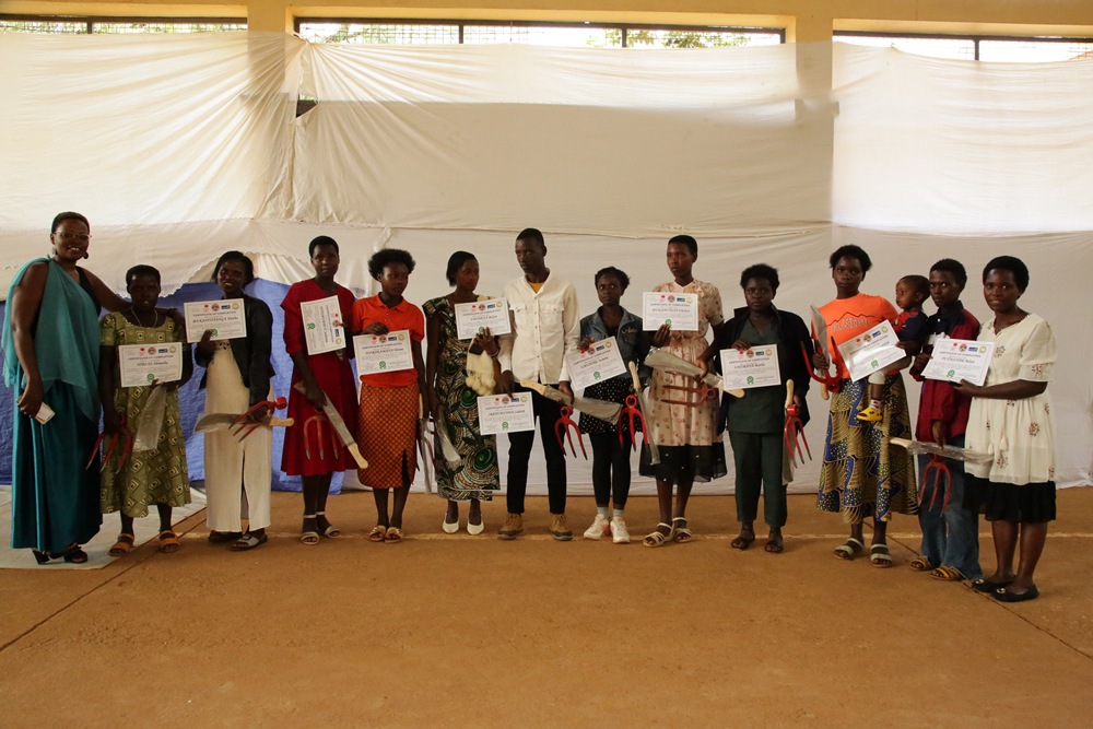 Group of children and two adults stand in a hall, each child holding a certificate during an award ceremony.
