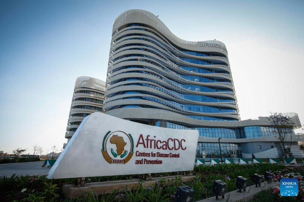 Modern curved glass-fronted Africa CDC headquarters with a large sign reading Africa CDC – Centres for Disease Control and Prevention in the foreground.