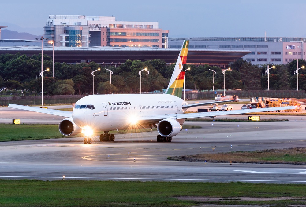Air Zimbabwe passenger jet taxiing on the runway at a modern airport, with terminal and trees in the background.
