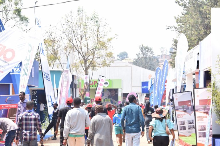 Crowd walking through an outdoor expo with colorful booths, banners, and displays on a sunny day.