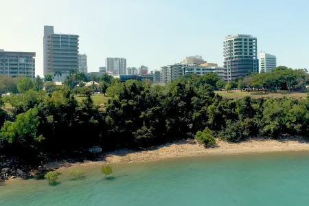 Riverfront park with trees and a city skyline of tall buildings in the distance.