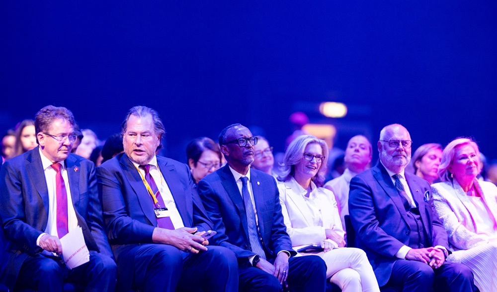 Group of professionally dressed attendees seated in a row at a conference under blue lighting.