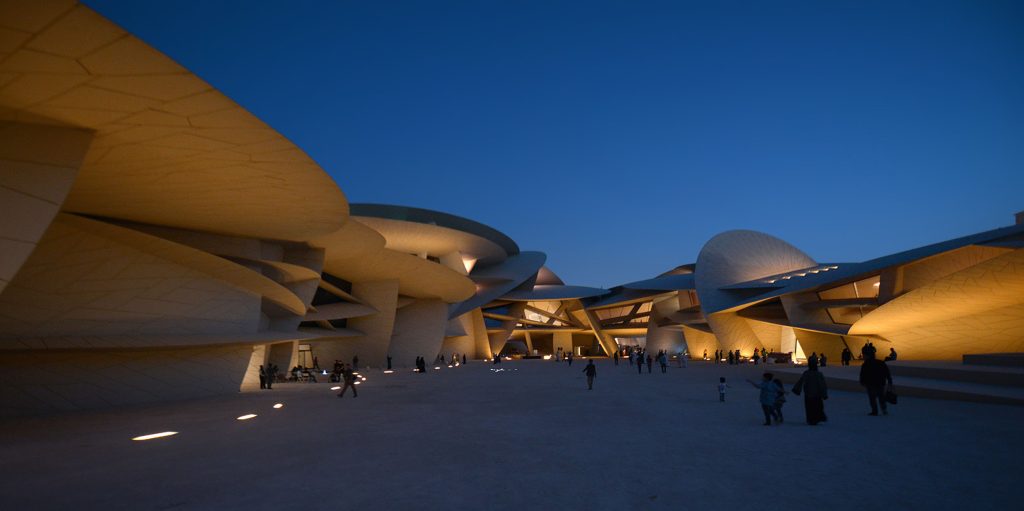 Evening view of Valencia's City of Arts and Sciences with futuristic white buildings and people walking among illuminated paths under a blue sky.