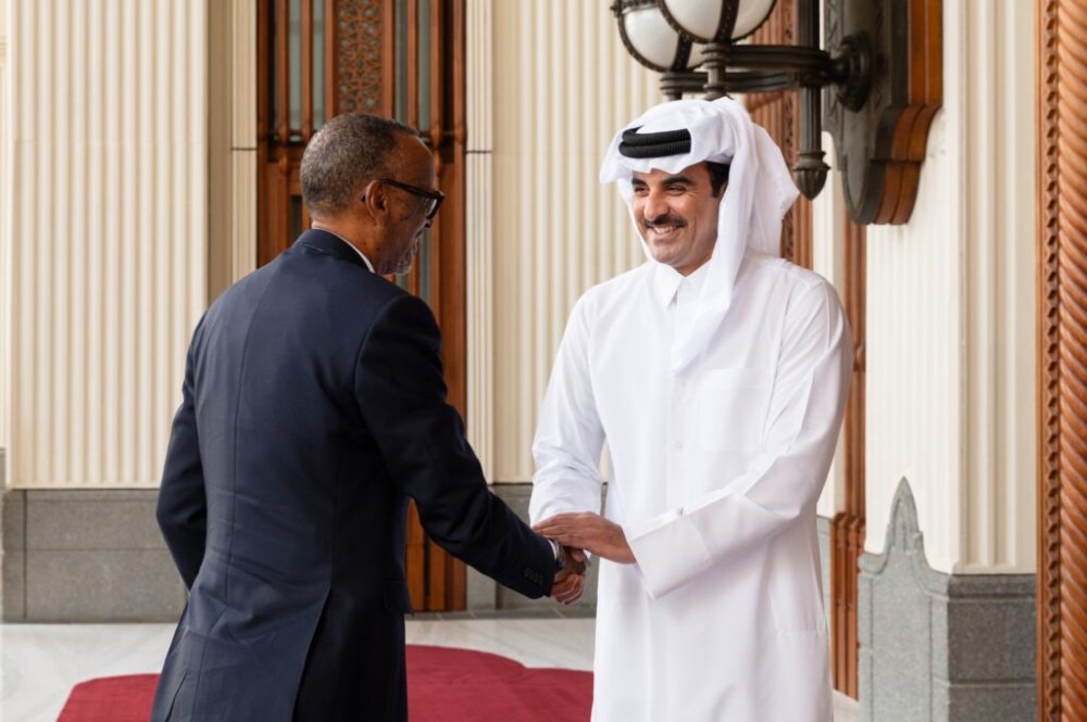 Two men shake hands in a formal setting; one in a dark suit and the other in white traditional Gulf attire, smiling at the entrance hall.