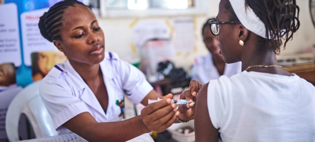Healthcare worker administering a vaccine shot to a patient in a clinic, both focused on the procedure