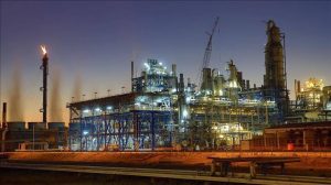 Industrial refinery complex at dusk with cranes, metal framework, and illuminated processing towers.